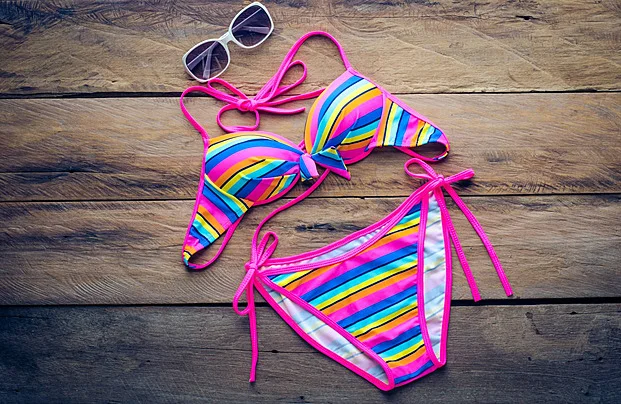 Bộ gái mặc bikini nhiều màu sắc với họa tiết sọc cầu vồng đặt trên sàn gỗ cùng kính râm