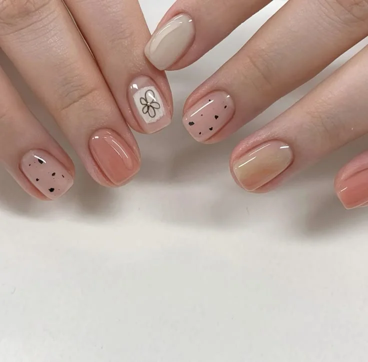Bộ nail sơn màu nude, cam đào và nâu đất, trang trí chấm bi đen và hình vẽ hoa đơn giản, tạo vẻ đẹp ngọt ngào, nữ tính.