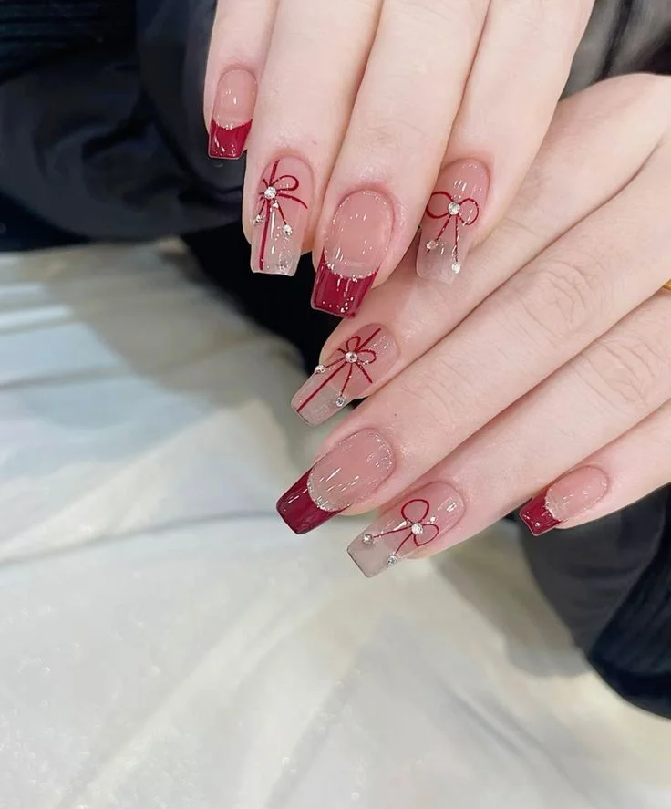 Bộ móng tay màu đỏ rượu và nude với các chi tiết nơ, kẻ sọc và viền đỏ, thiết kế móng tay đẹp.