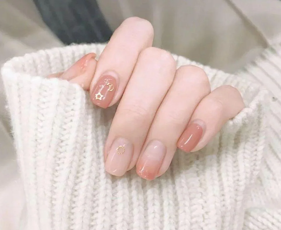 Bộ móng tay màu nude trong suốt với các chi tiết hình sao và đường kẻ vàng tinh tế, thiết kế móng tay đẹp.